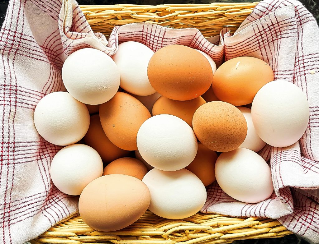 brown and white eggs in whicker basket lined with plaid fabric