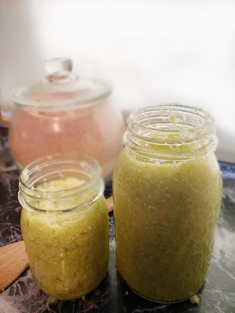 two jars of homemade sauerkraut with large jar of salt in the background