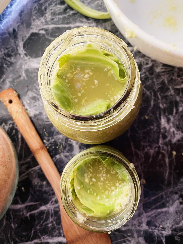 two mason jars of homemade sauerkraut with extra cabbage leaves folded on top
