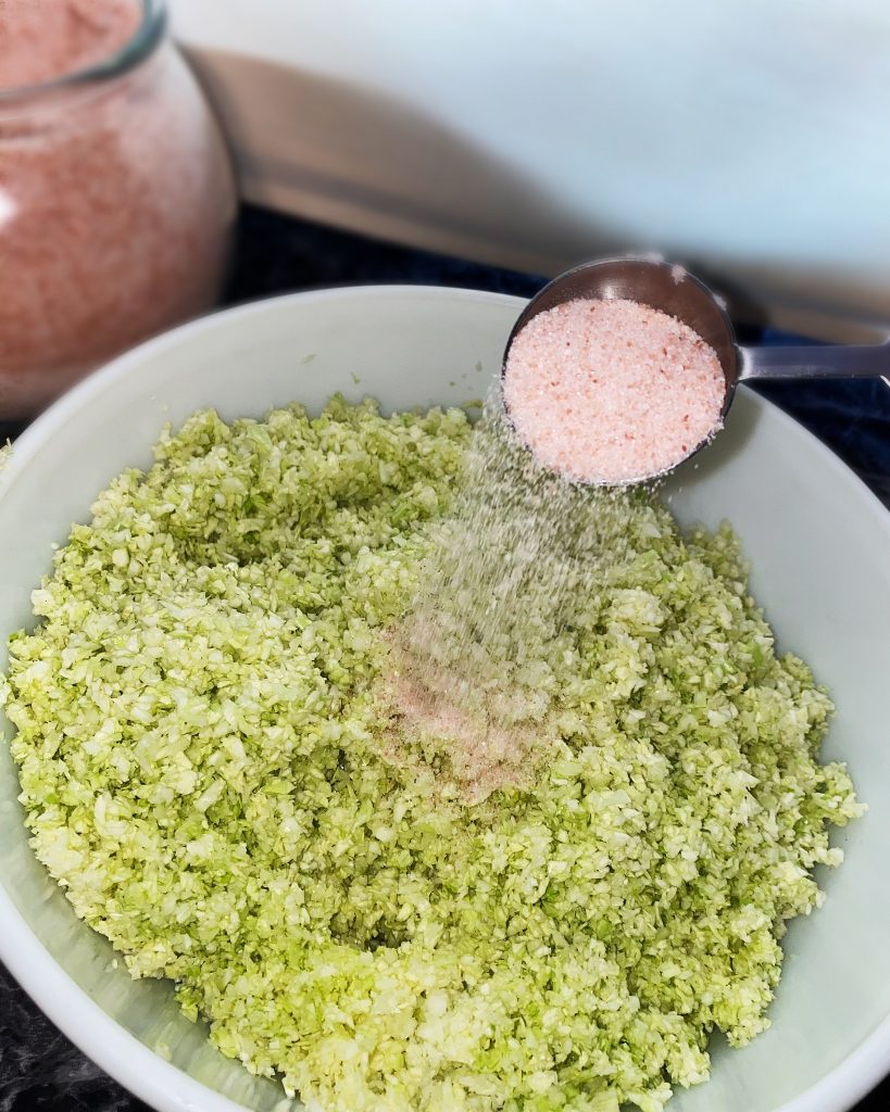 pink Himalayan salt being dumped into shredded cabbage in mixing bowl