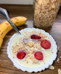 small white bowl filled with yogurt, strawberries, milled flax seeds, and almonds.